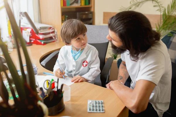 Kleine jongen spelen doet alsof als dokter onderzoeken van een man in comfortabele medische kantoor — Stockfoto