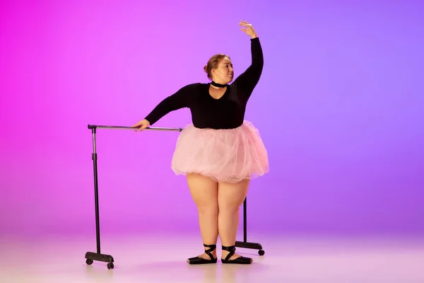 Bonito caucasiano plus size modelo praticando dança de balé em gradiente roxo-rosa estúdio fundo em luz de néon — Fotografia de Stock