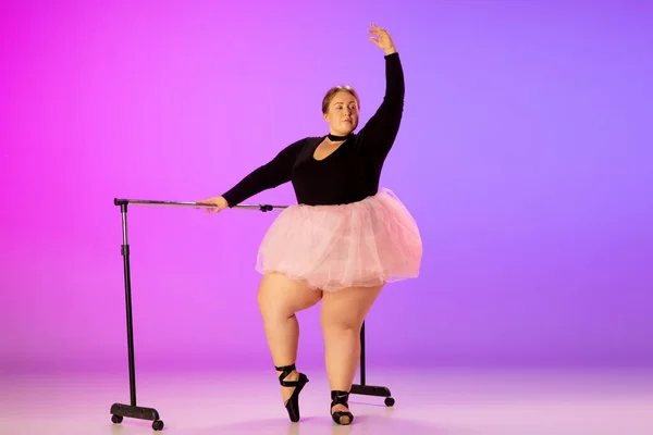 Bonito caucasiano plus size modelo praticando dança de balé em gradiente roxo-rosa estúdio fundo em luz de néon — Fotografia de Stock