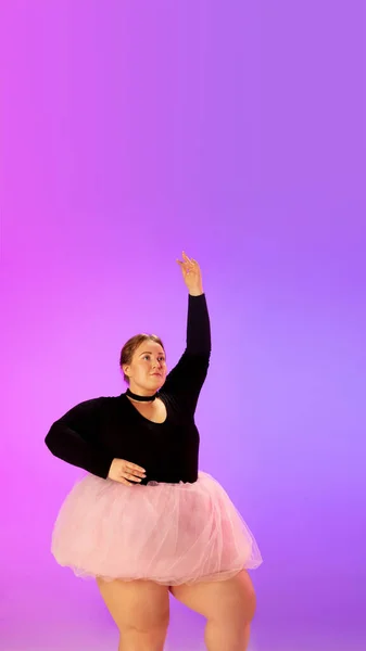 Красива кавказька модель плюс розмір, що практикує балетний танець на градієнтному фіолетово-рожевому студійному фоні в неоновому світлі — стокове фото