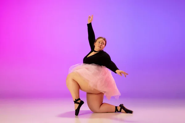 Hermosa modelo caucásica más tamaño practicando danza de ballet en degradado púrpura-rosa fondo del estudio en luz de neón —  Fotos de Stock