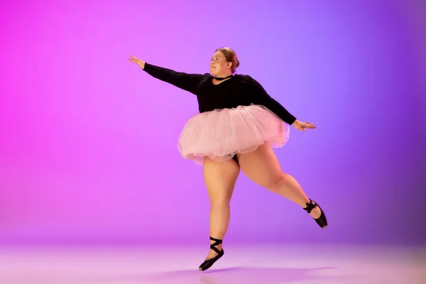 Bonito caucasiano plus size modelo praticando dança de balé em gradiente roxo-rosa estúdio fundo em luz de néon — Fotografia de Stock