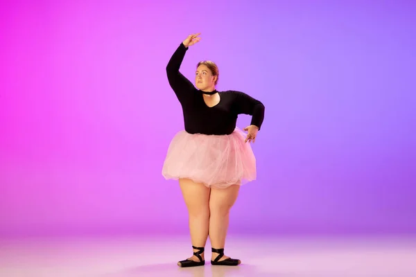 Bonito caucasiano plus size modelo praticando dança de balé em gradiente roxo-rosa estúdio fundo em luz de néon — Fotografia de Stock