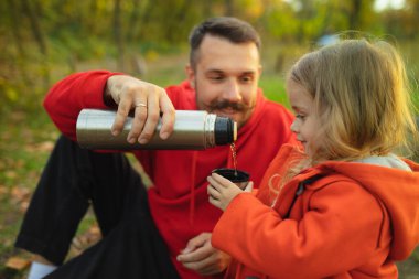 Mutlu baba ve küçük tatlı kız sonbahar güneşli bir günde orman yolunda yürüyorlar.