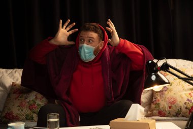 Ekoseli bir maske takmış bir adam hasta birinden korumaya çalışıyor.