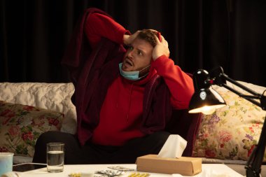 Ekoseli bir maske takmış bir adam hasta birinden korumaya çalışıyor.