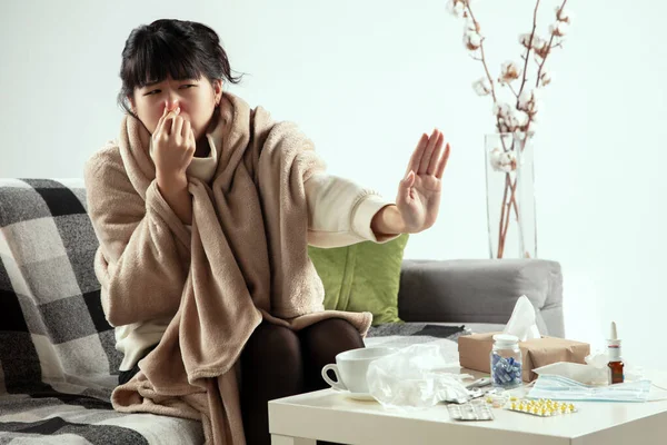 Žena zabalená v kostkovaném plášti vypadá nemocná, nemocná, kýchá a kašle, sedí doma — Stock fotografie