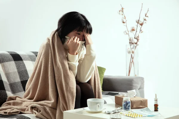 Femme enveloppée dans un plaid semble malade, malade, éternuer et tousser assis à la maison à l'intérieur — Photo