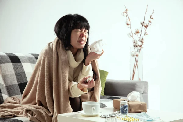 Woman wrapped in a plaid looks sick, ill, sneezing and coughing sitting at home indoors — Stock Photo, Image