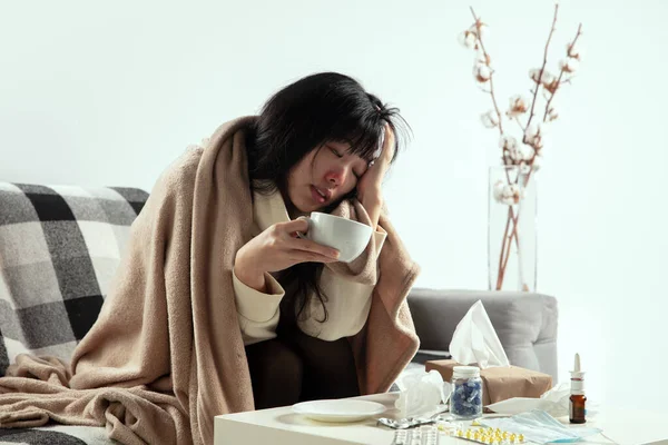 Femme enveloppée dans un plaid semble malade, malade, éternuer et tousser assis à la maison à l'intérieur — Photo