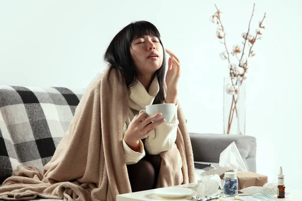 Kvinna insvept i en rutig ser sjuk, sjuk, nysningar och hosta sitter hemma — Stockfoto