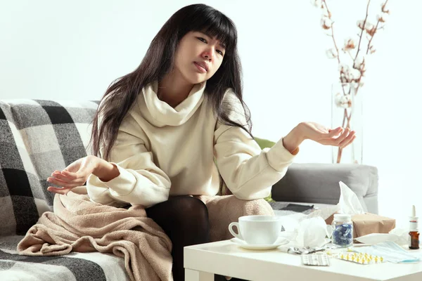 Woman wrapped in a plaid looks sick, ill, sneezing and coughing sitting at home indoors