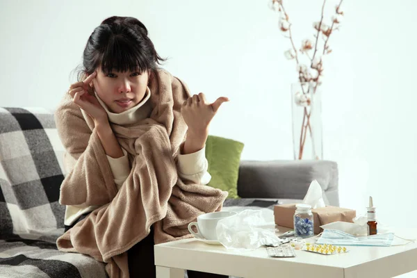 Žena zabalená v kostkovaném plášti vypadá nemocná, nemocná, kýchá a kašle, sedí doma — Stock fotografie