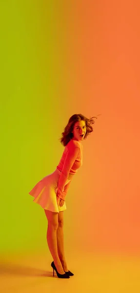 Vacker förförisk flicka i fashionabla, romantiska outfit på ljus lutning grön-orange bakgrund i neon ljus — Stockfoto