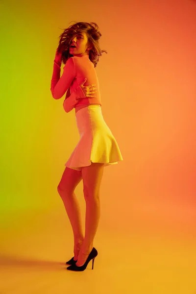 Mooi verleidelijk meisje in modieuze, romantische outfit op heldere gradiënt groen-oranje achtergrond in neon licht — Stockfoto
