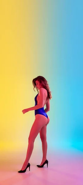 Beautiful seductive girl in fashionable blue swimsuit on bright gradient yellow-blue background in neon light — Stock Photo, Image