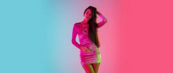 Beautiful seductive girl in fashionable dress, outfit on bright gradient pink-blue background in neon light — Stock Photo, Image
