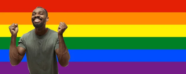 Молодий дивовижний афро-американський чоловік на різнокольоровому фоні, утворюючи прапор гордості — стокове фото