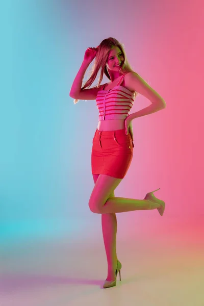 Mooi meisje in modieuze, romantische outfit op heldere gradiënt roze-blauwe achtergrond in neon licht — Stockfoto