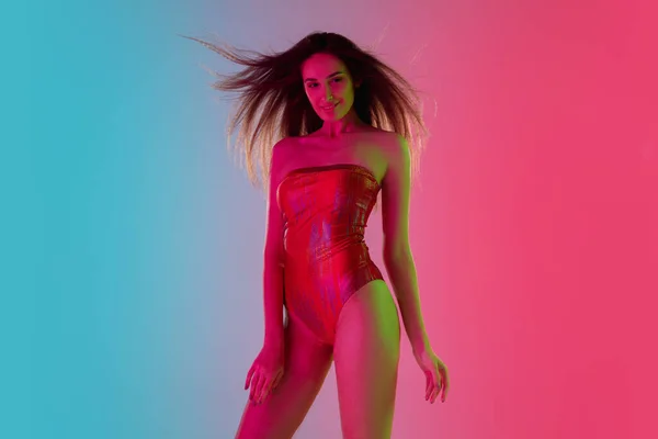 Menina sedutora bonita em maiô vermelho na moda em gradiente brilhante fundo rosa-azul em luz de néon — Fotografia de Stock