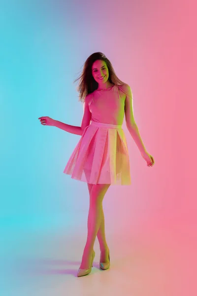 Mooi verleidelijk meisje in modieuze, romantische outfit op heldere gradiënt roze-blauwe achtergrond in neon licht — Stockfoto