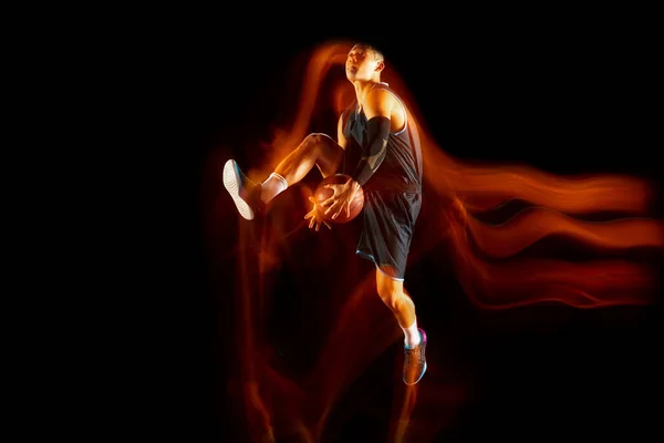 Jonge Oost-Aziatische basketbalspeler in actie en spring in gemengd licht over donkere studio-achtergrond. Begrip sport, beweging, energie en dynamische, gezonde levensstijl. — Stockfoto