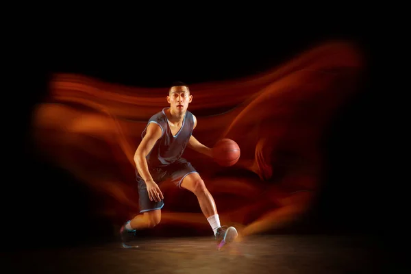 Jovem jogador de basquete asiático leste em ação e saltar em luz mista sobre fundo estúdio escuro. Conceito de esporte, movimento, energia e estilo de vida dinâmico e saudável. — Fotografia de Stock