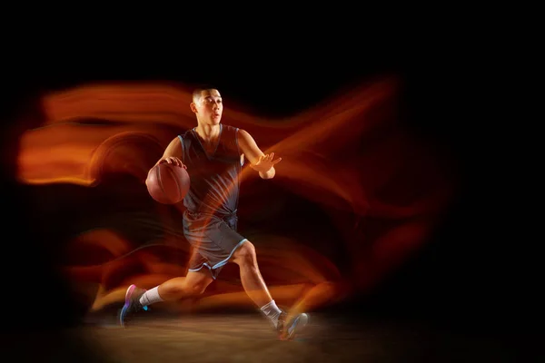 年轻的东亚篮球运动员在行动中,在黑暗的工作室背景下,在混光中跳跃.体育、运动、精力和充满活力、健康的生活方式的概念. — 图库照片