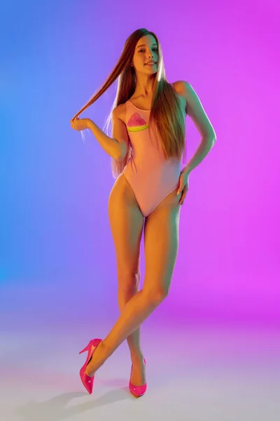Hermosa chica seductora en traje de baño rosa de moda sobre brillante degradado púrpura-azul de fondo en luz de neón —  Fotos de Stock