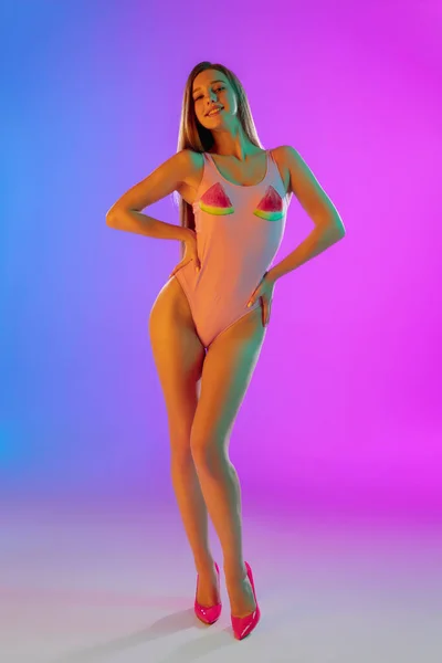 Hermosa chica seductora en traje de baño rosa de moda sobre brillante degradado púrpura-azul de fondo en luz de neón —  Fotos de Stock