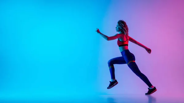 Jovem mulher esportiva correndo isolado no gradiente rosa-azul estúdio fundo em luz de néon. — Fotografia de Stock