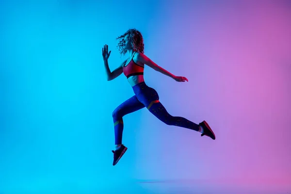 Wanita muda sportif berjalan terisolasi pada gradien pink-biru studio latar belakang dalam cahaya neon. — Stok Foto