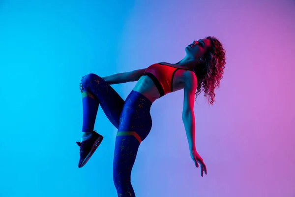 Retrato de una joven hermosa mujer en ropa deportiva brillante aislado en degradado rosa-azul fondo del estudio en luz de neón. —  Fotos de Stock