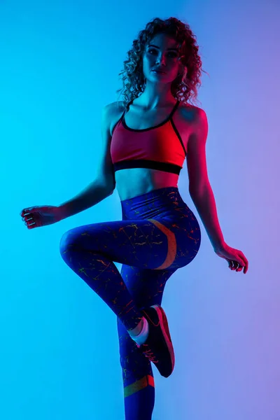 Jovem esportivo mulher formação isolada no gradiente rosa-azul estúdio fundo em luz de néon. — Fotografia de Stock