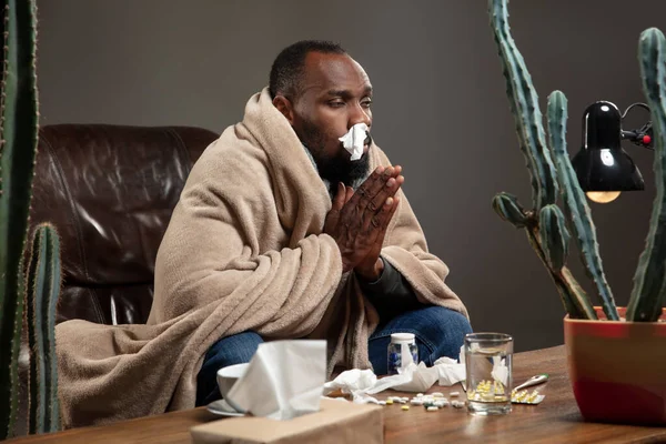 Ung afro-amerikan insvept i en rutig ser sjuk ut, sjuk sittande hemma. — Stockfoto