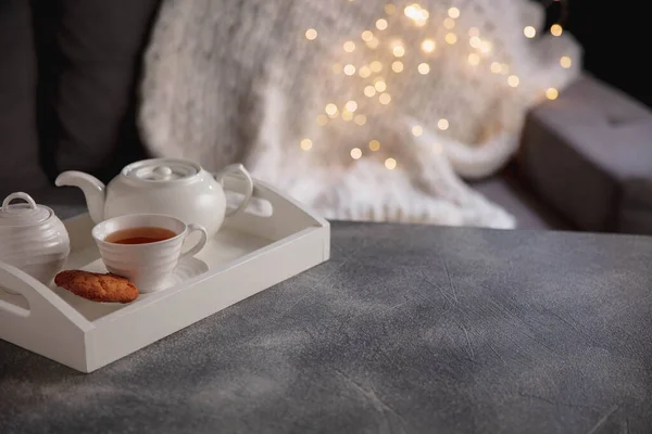 Acogedor invierno. Bandeja de madera blanca con juego de té sobre mesa gris con luces de guirnalda led. El concepto de ambiente hogareño y confort. — Foto de Stock