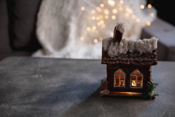 Casa miniatura iluminada sobre fondo gris. Acogedor invierno, nevando. Copiar el espacio para el anuncio, diseño. — Foto de Stock