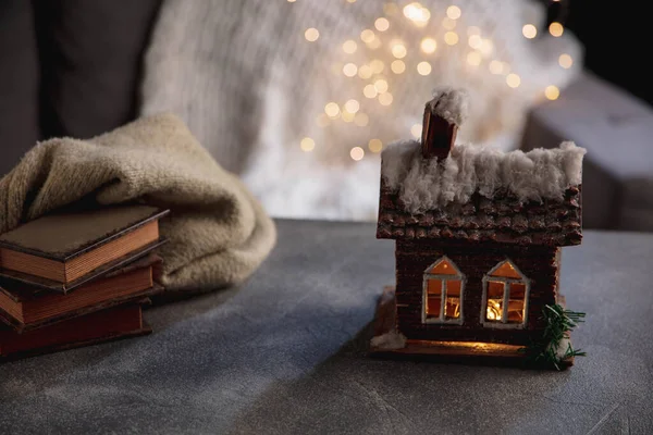 Casa de invierno miniatura iluminada y libros sobre fondo gris y blanco. El concepto de ambiente hogareño y confort. — Foto de Stock