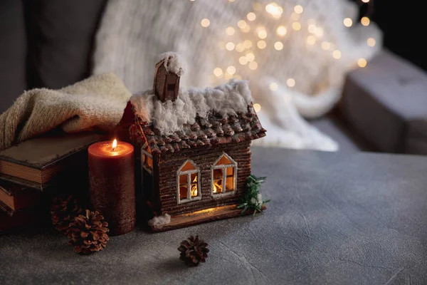Casa de invierno miniatura iluminada y libros sobre fondo gris y blanco. El concepto de ambiente hogareño y confort. — Foto de Stock
