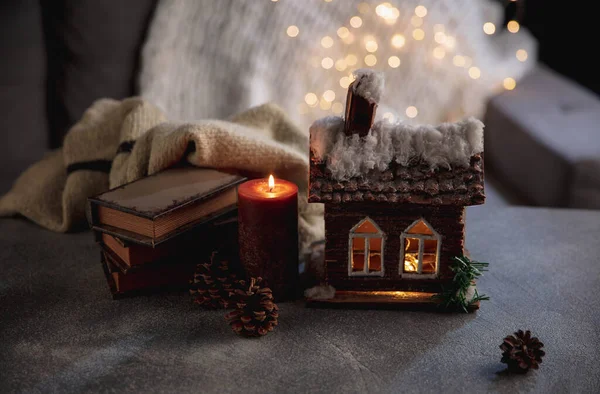 Casa de invierno miniatura iluminada y libros sobre fondo gris y blanco. El concepto de ambiente hogareño y confort. — Foto de Stock