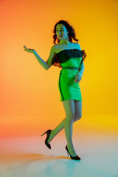 Vacker förförisk flicka i fashionabla, moderna outfit på ljusa lutning gul-orange bakgrund i neon ljus — Stockfoto