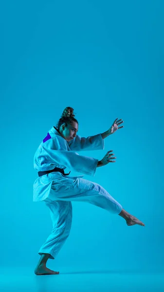 Jonge meisje professionele judoist geïsoleerd op blauwe studio achtergrond in neon licht. Gezonde levensstijl, sportconcept. — Stockfoto