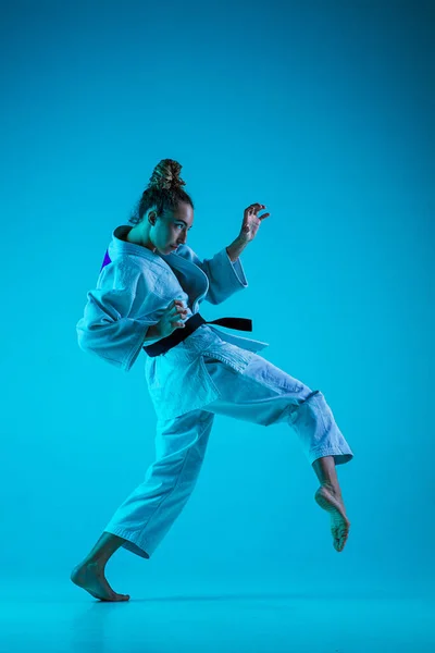 Jonge meisje professionele judoist geïsoleerd op blauwe studio achtergrond in neon licht. Gezonde levensstijl, sportconcept. — Stockfoto