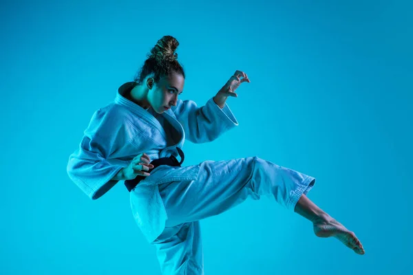 Jovencita judoista profesional aislado en fondo de estudio azul en luz de neón. Estilo de vida saludable, concepto deportivo. — Foto de Stock