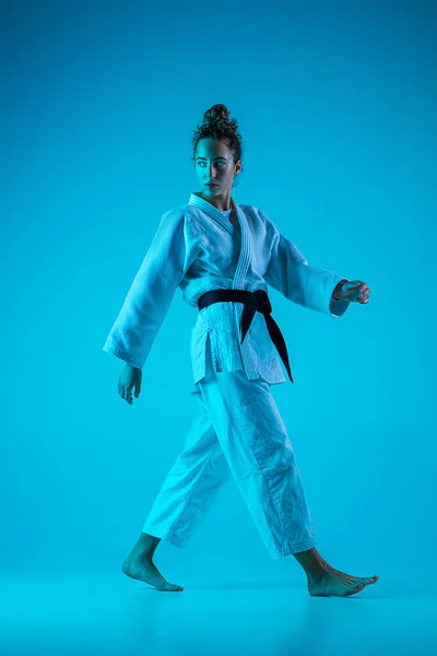 Judoista femenina profesional posando aislada sobre fondo de estudio azul en luz de neón. Estilo de vida saludable, concepto deportivo. —  Fotos de Stock