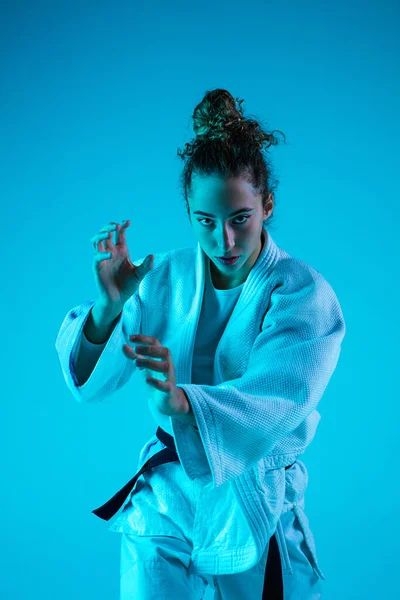 Jonge meisje professionele judoist geïsoleerd op blauwe studio achtergrond in neon licht. Gezonde levensstijl, sportconcept. — Stockfoto