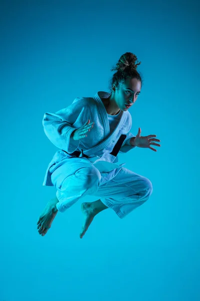 Jonge meisje professionele judoist geïsoleerd op blauwe studio achtergrond in neon licht. Gezonde levensstijl, sportconcept. — Stockfoto