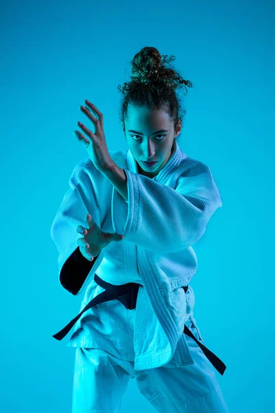 Jonge meisje professionele judoist geïsoleerd op blauwe studio achtergrond in neon licht. Gezonde levensstijl, sportconcept. — Stockfoto