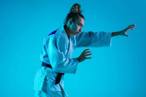 Professionele vrouwelijke judoïstische training geïsoleerd op blauwe studio achtergrond in neon licht. Gezonde levensstijl, sportconcept. — Stockfoto