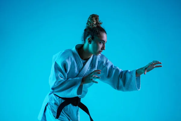 Professional female judoist training isolated on blue studio background in neon light. Healthy lifestyle, sport concept.